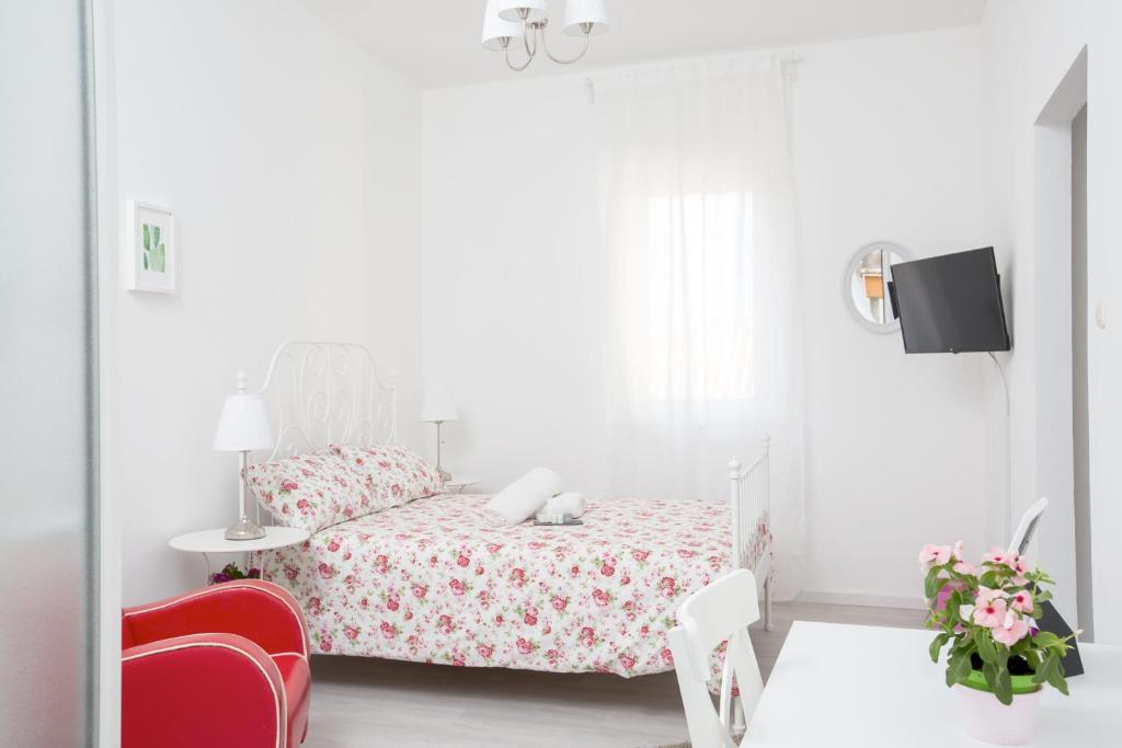 a white bedroom with a bed and a red chair at Maison Ortigia in Syracuse