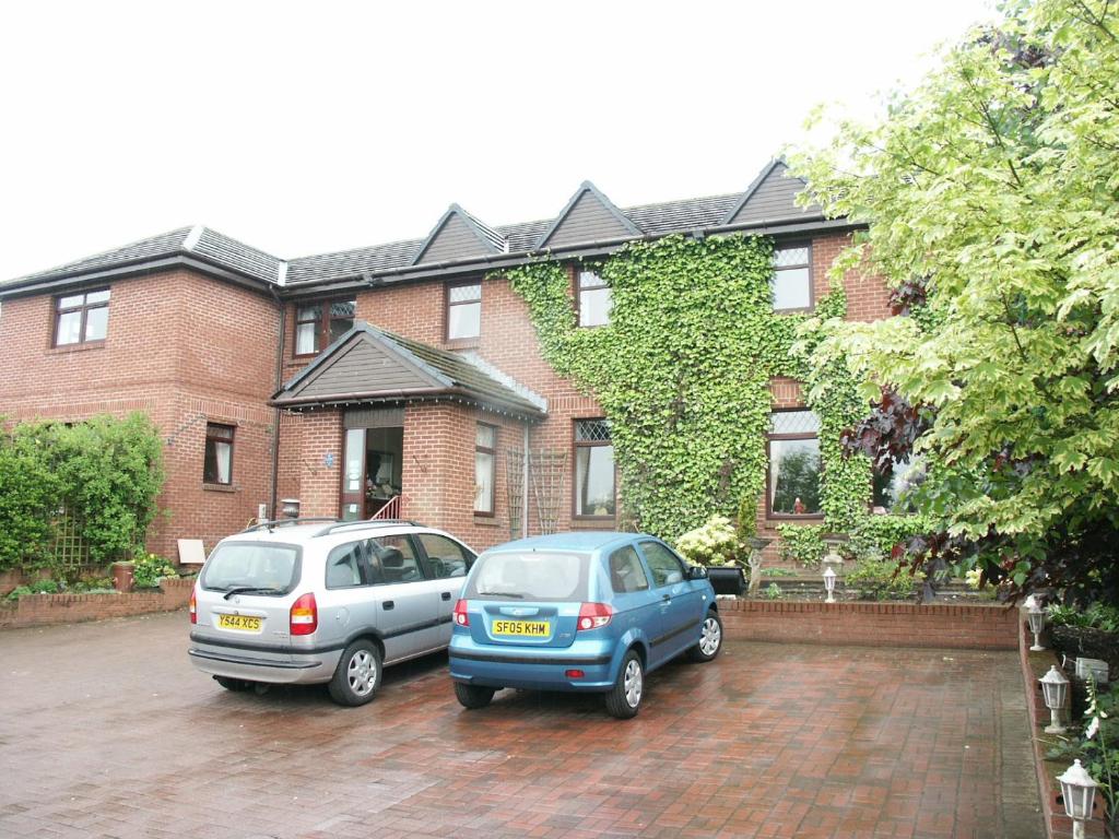 dos autos estacionados frente a una casa de ladrillo en Herdshill Guest House, en Wishaw