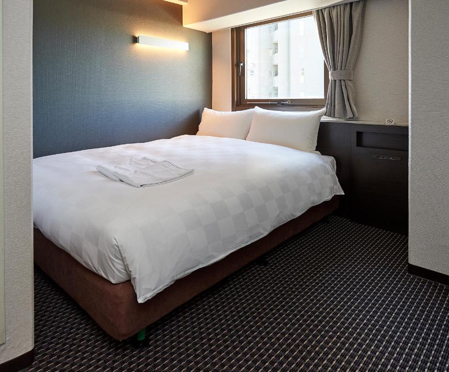 a bedroom with a large white bed with a window at Hotel Consort Shin-Osaka in Osaka