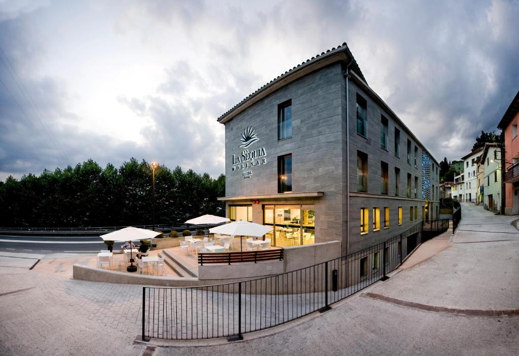 un bâtiment avec des tables et des parasols devant lui dans l'établissement Hotel La Sèquia Molinar, à Campdevánol