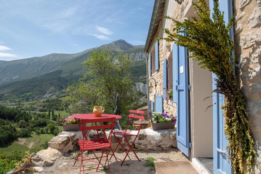 Gaïa, maison d'hôtes Verdon, vue féerique في Blieux: طاولة حمراء وكراسي على شرفة مع الجبال