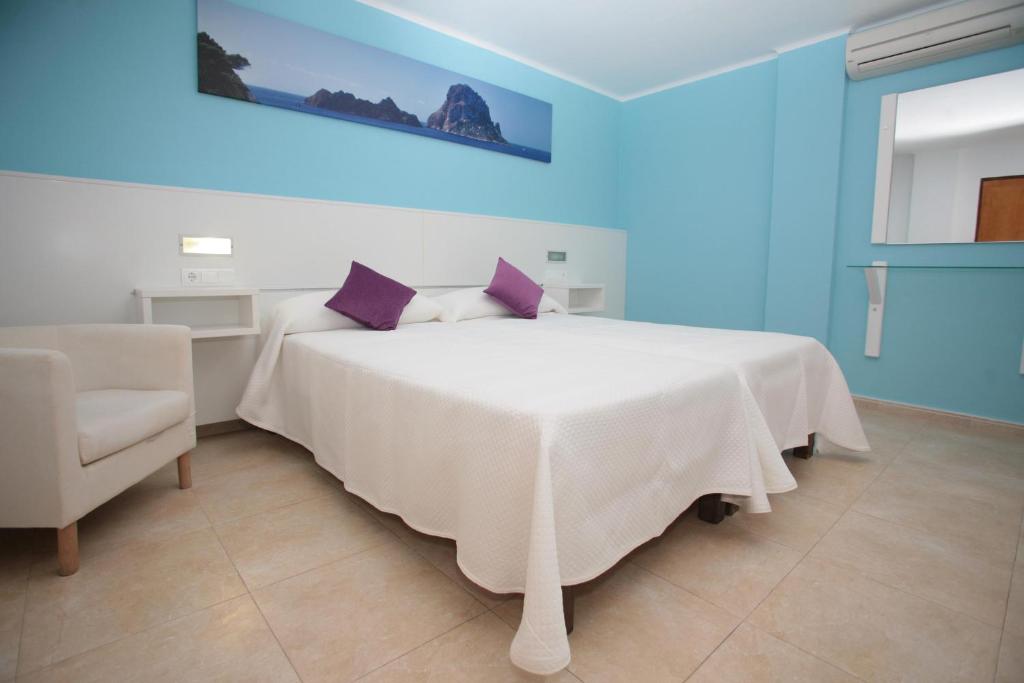 Un dormitorio con una cama blanca con almohadas moradas y una silla en Hostal Costa Blanca, en Ibiza