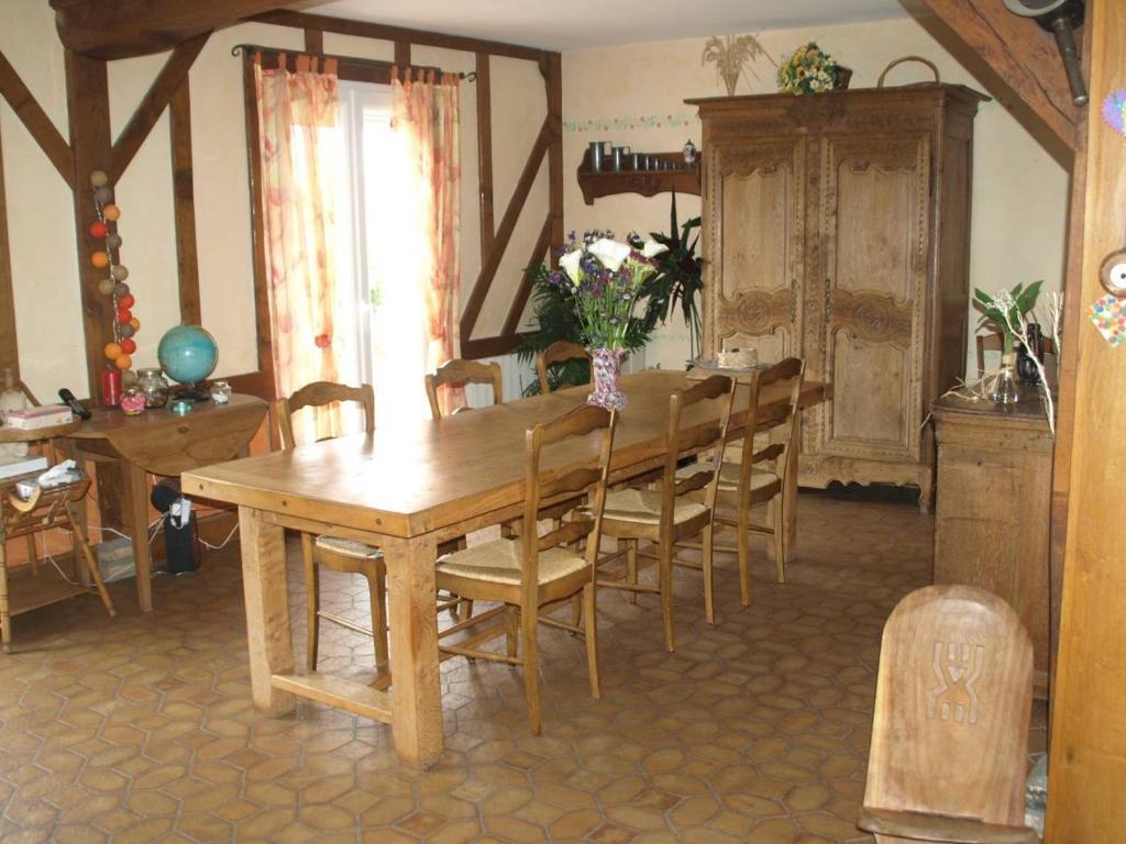 een houten eettafel met stoelen en een vaas met bloemen bij La Risloise in Corneville-sur-Risle