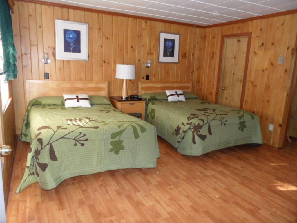two beds in a room with wooden walls and wood floors at Seven Dwarfs Motel & Cabins in Lake George