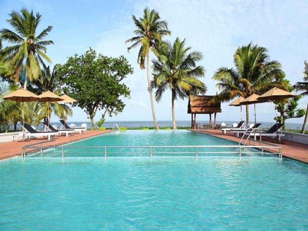 a large swimming pool with chairs and umbrellas at Abad Whispering Palms in Kumarakom