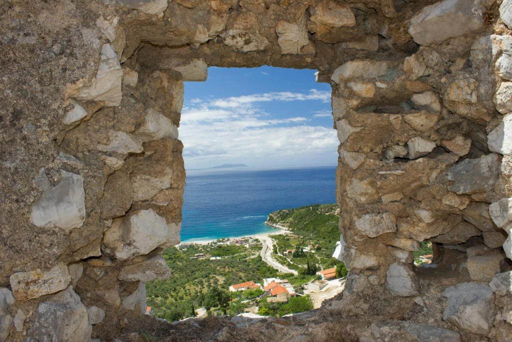 a window in a stone wall looking at the ocean at Himara Hostel in Himare