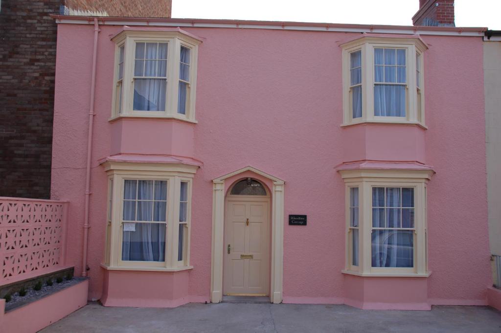 テンビーにあるWoodbine Cottageの白いドアと窓のあるピンクの家