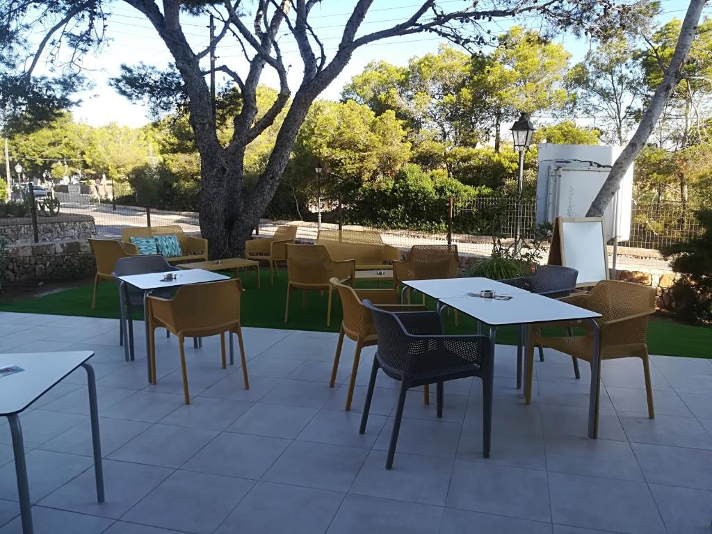 a patio with tables and chairs and a tree at Apartamentos Villa Primera in Cala Figuera