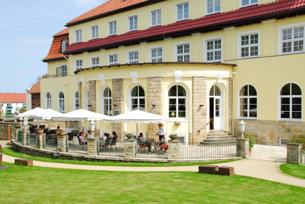 un edificio con gente sentada bajo sombrillas delante de él en Kurhotel Fürstenhof by David, en Blankenburg