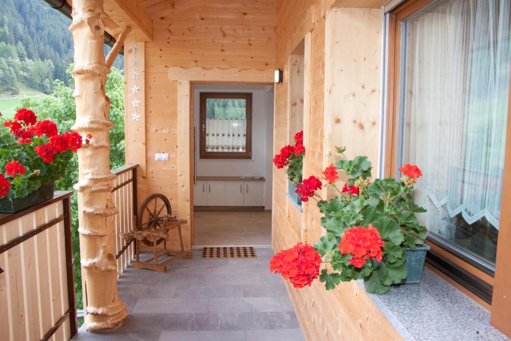 un porche con geranios rojos en una casa de madera en Schweinsteghof Urlaub auf dem Bauernhof, en Sarentino