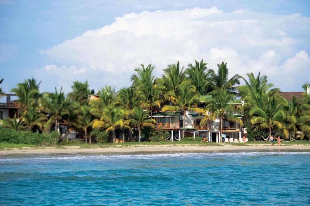 a resort on a beach with palm trees and the water at La Casa de Marita in Puerto Villamil