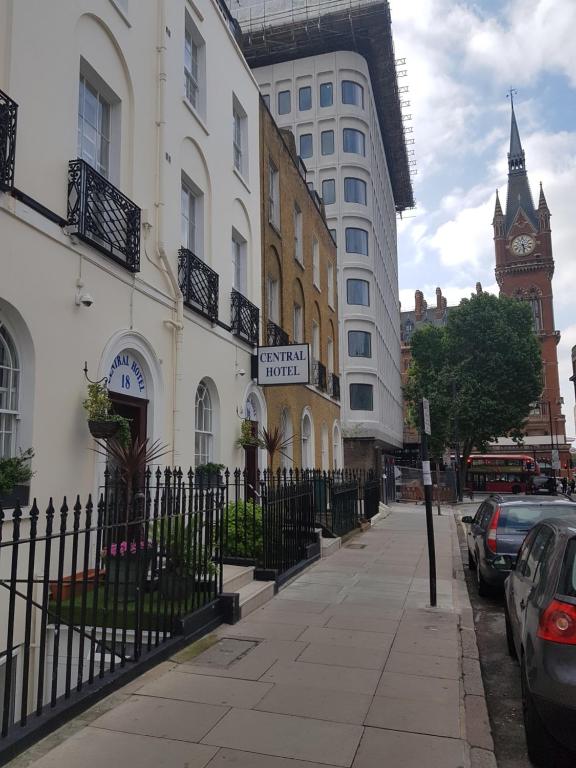 una strada cittadina con recinzione in ferro battuto e torre dell'orologio di Central Hotel a Londra