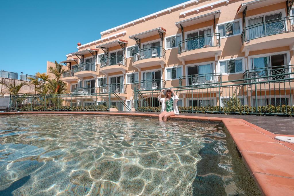 uma menina de pé em uma piscina em um hotel em Il Palazzo Holiday Apartments em Cairns