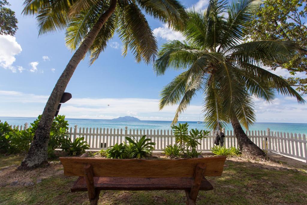 a wooden bench sitting under two palm trees near the ocean at Sables d'Or Luxury Apartments in Beau Vallon
