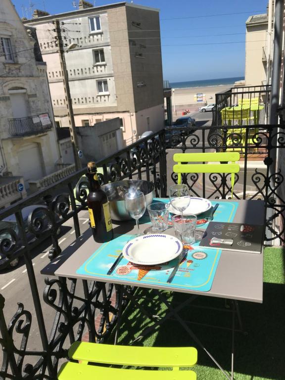 une table avec des assiettes et des verres à vin sur un balcon dans l'établissement Appartement à 30 m de la plage - balcon - lumineux - wifi - Le Cérès 2, à Berck-sur-Mer