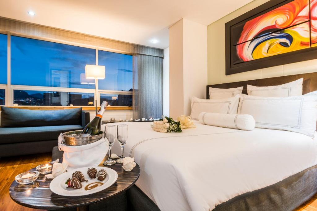 Una habitación de hotel con una cama y una mesa con una botella de vino en One Sixteen Hotel en Bogotá