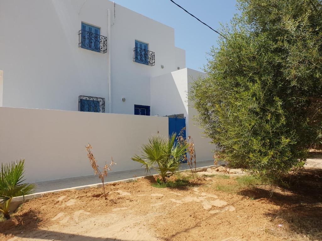 a white building with blue windows and a tree at Menzel Rayan in Midoun
