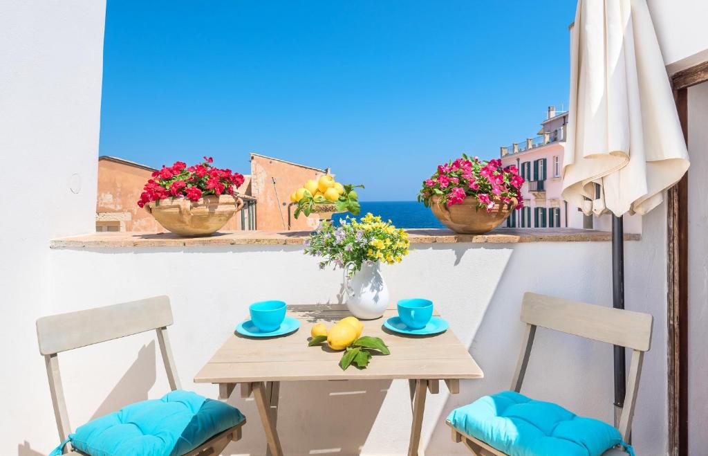 una mesa con sillas y flores en el balcón en La Gorgone Ortigia Apartments, en Siracusa