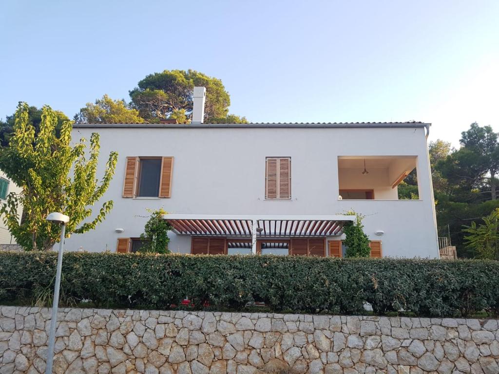 une maison blanche avec une haie devant elle dans l'établissement Apartman Di, à Mali Lošinj