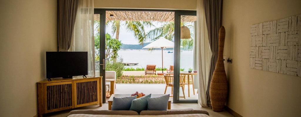 a living room with a couch and a television and a patio at Que Toi Village Resort Phu Yen in Song Cau