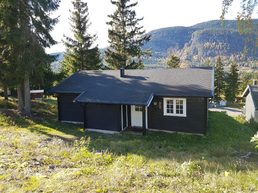 a small black house in a field with trees at Sørlia hytte in Hafjell