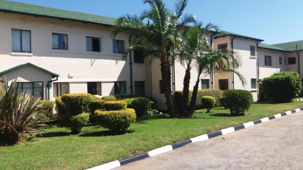 un bâtiment avec un palmier et des buissons dans une cour dans l'établissement Montclair Hotel and Casino, à Nyanga