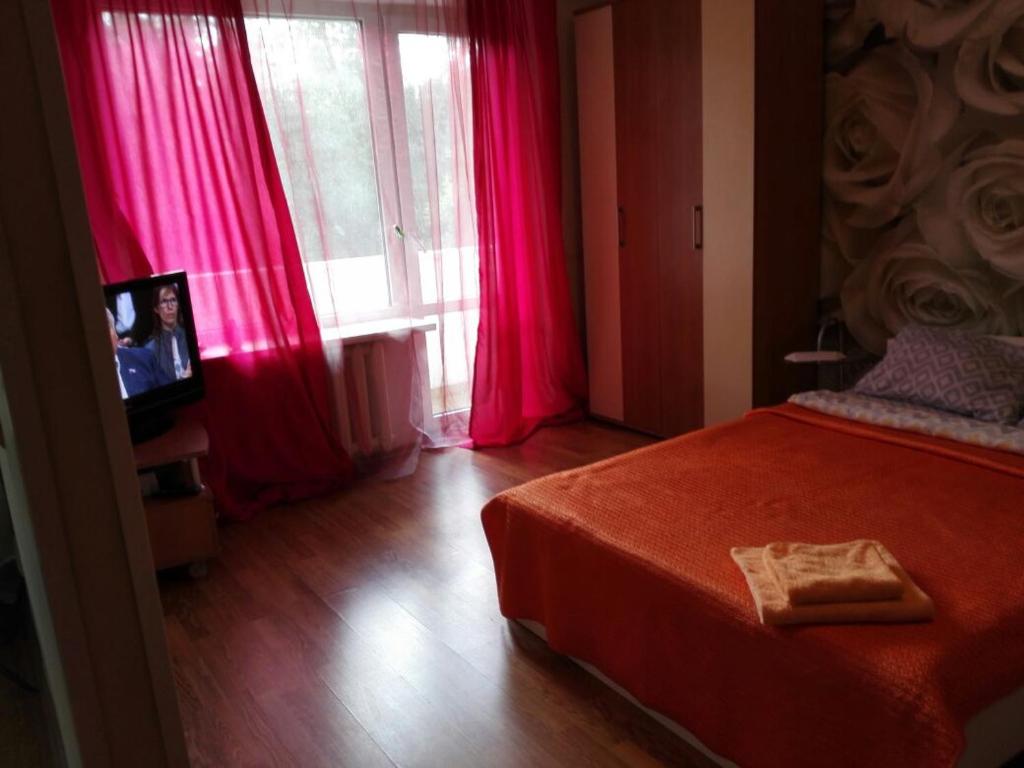 モスクワにあるApart Центр Zooのピンクのカーテン、ベッド、テレビが備わるベッドルーム1室が備わります。