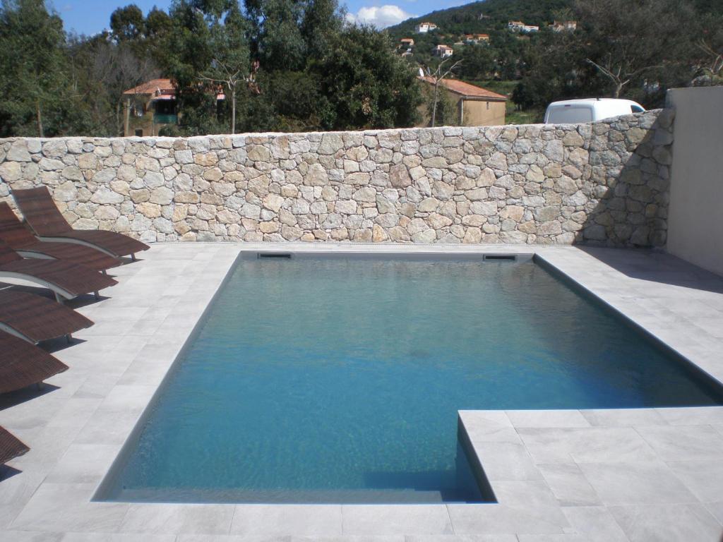 a swimming pool in front of a stone wall at Hôtel l'Alivu in Galeria