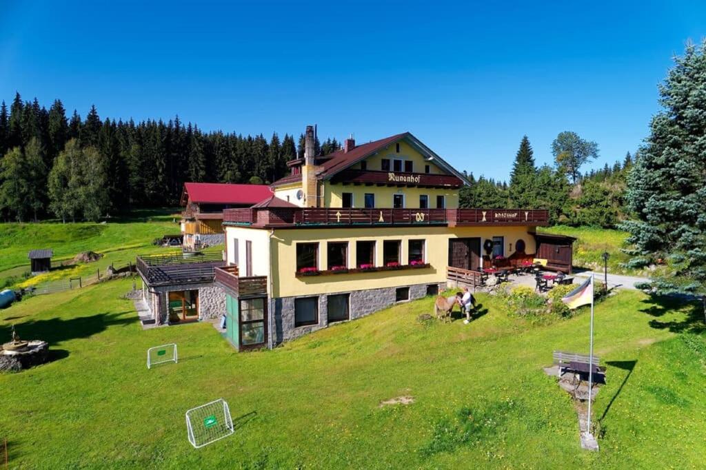 a large house on top of a green hill at Bauernhofpension Runenhof in Haidmühle