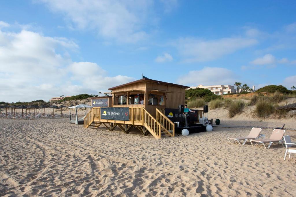 a house on the beach with chairs and a building at Hipotels Playa La Barrosa - Adults Only in Chiclana de la Frontera