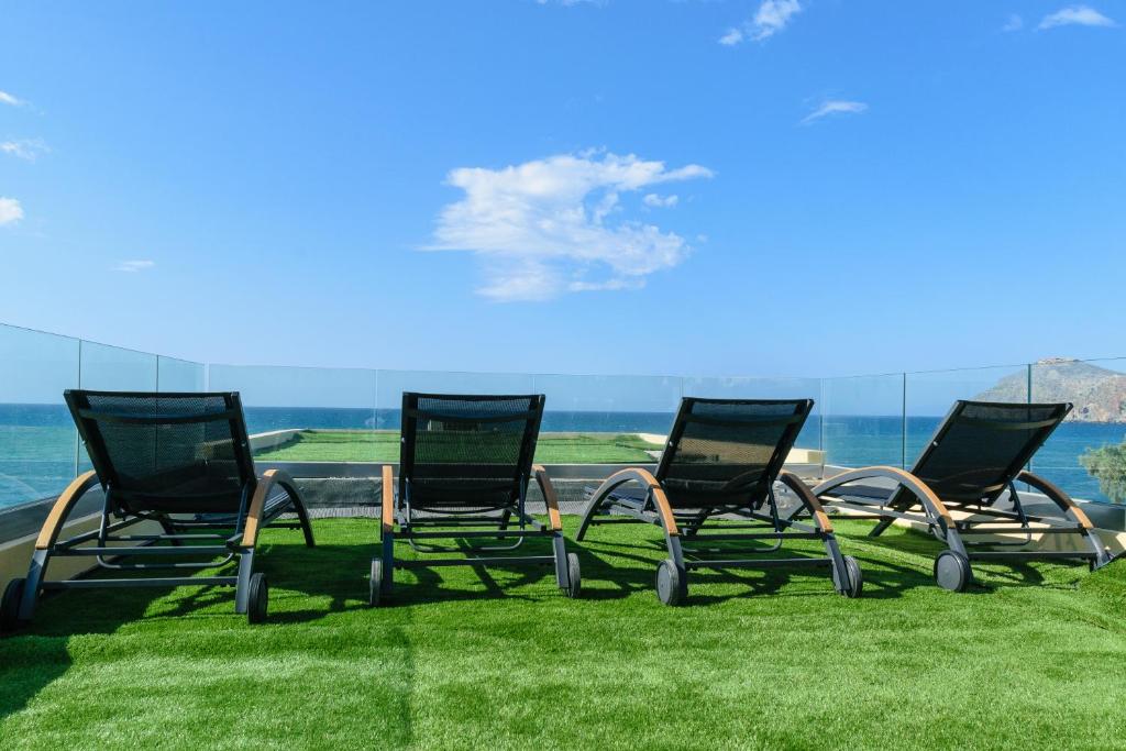 a group of chairs sitting on the grass near the water at Aetheras Beach in Platanias