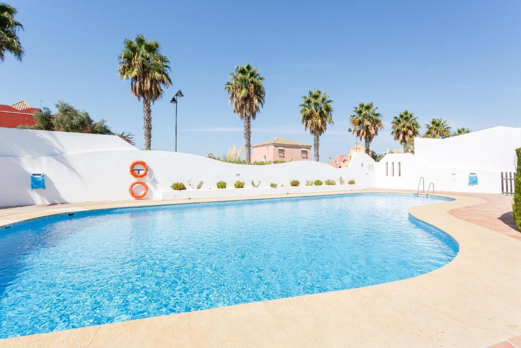 サンルーカル・デ・バラメダにあるBonito apartamento en campo de golf con piscinaのヤシの木が背景に浮かぶスイミングプール