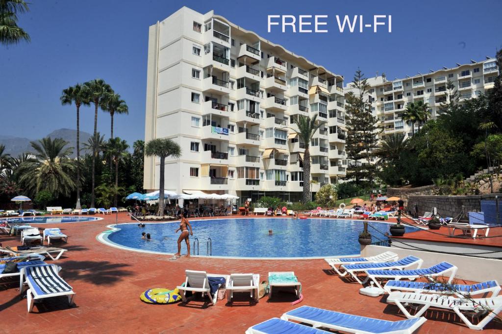 ein Hotel mit einem Pool mit Stühlen und einer Frau davor in der Unterkunft eldorado blue in Playa de las Americas