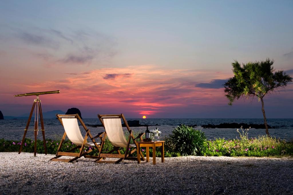 2 sillas y una mesa en la playa al atardecer en Nefeli Sunset Studios, en Pollonia