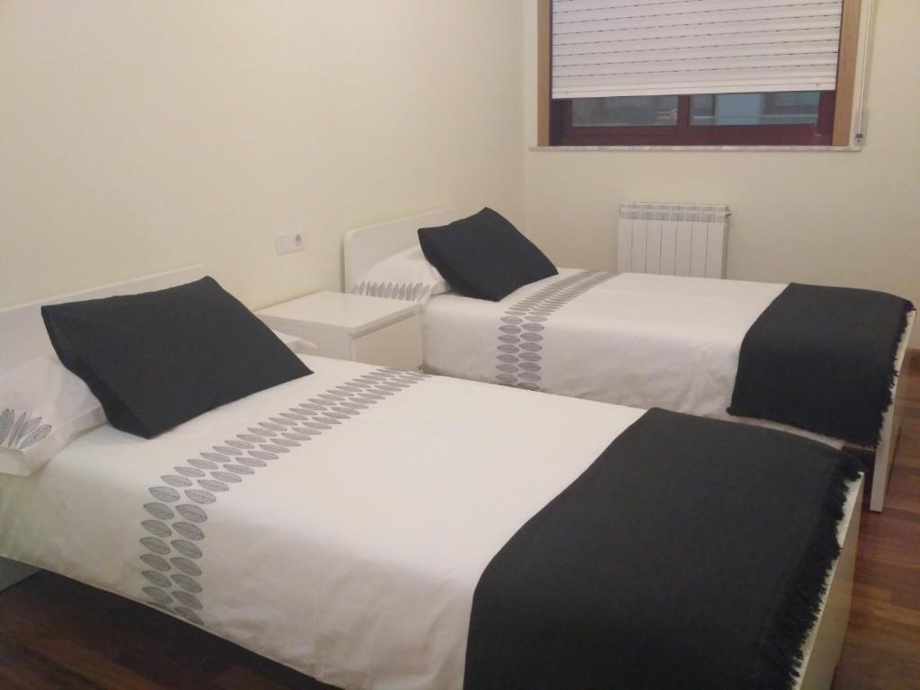 2 Betten mit schwarzer und weißer Bettwäsche in einem Zimmer in der Unterkunft Apartamento Lua in O Milladoiro