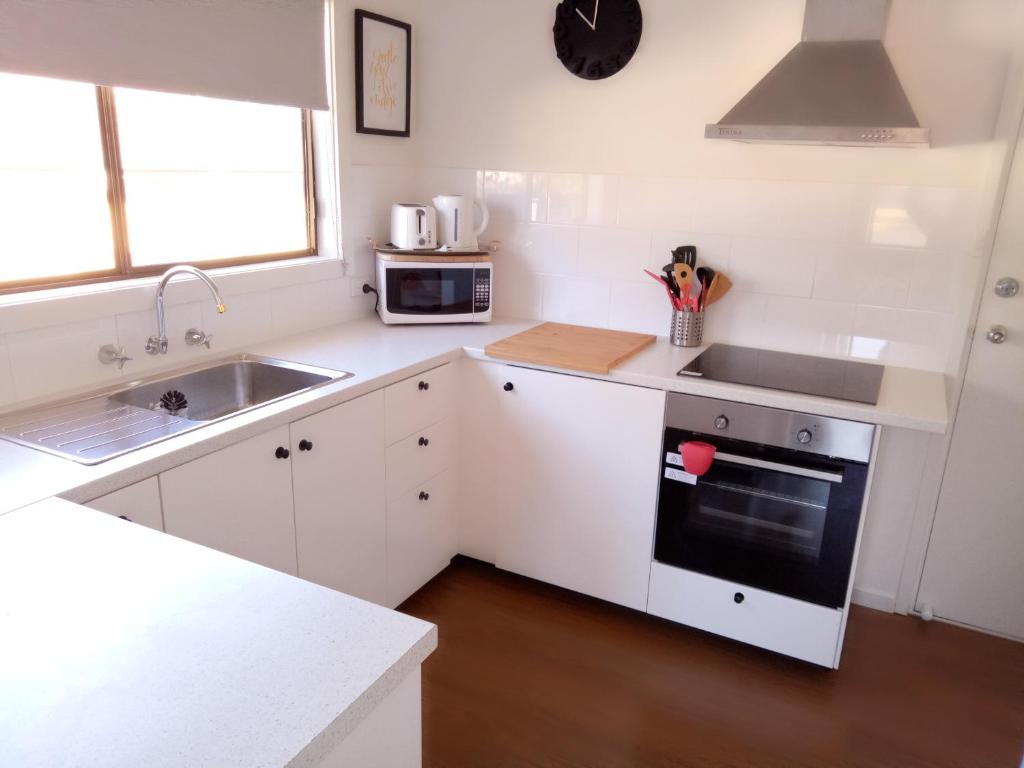 a white kitchen with a sink and a stove at The Husky House or The Husky Studio Suite stayinjervisbay com in Huskisson