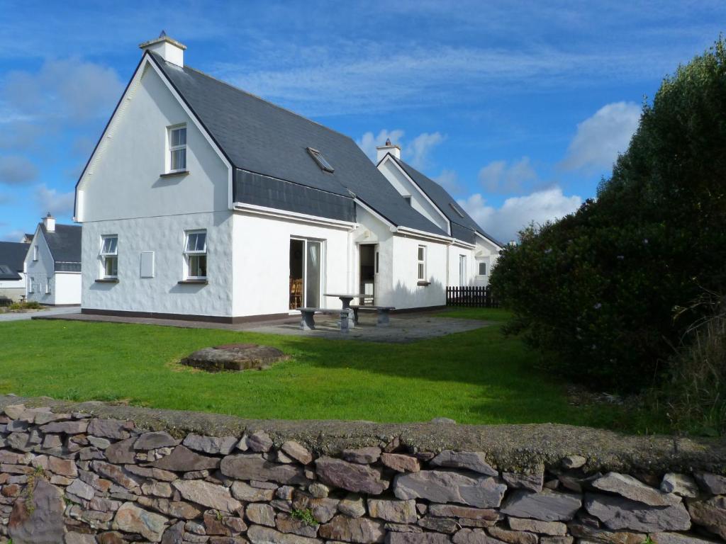a white house with a stone wall in front of it at Skellig Cottages in Ballinskelligs