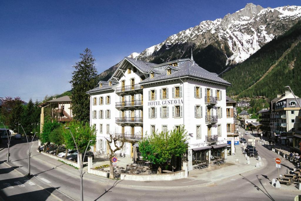a large white building in front of a mountain at Langley Hotel Gustavia in Chamonix