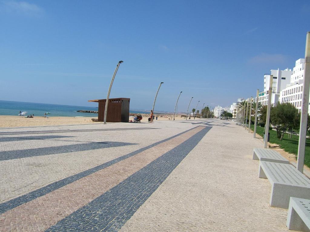 eine Straße mit Bänken und ein Strand mit Gebäuden in der Unterkunft Varandas de Carteia G/F in Quarteira
