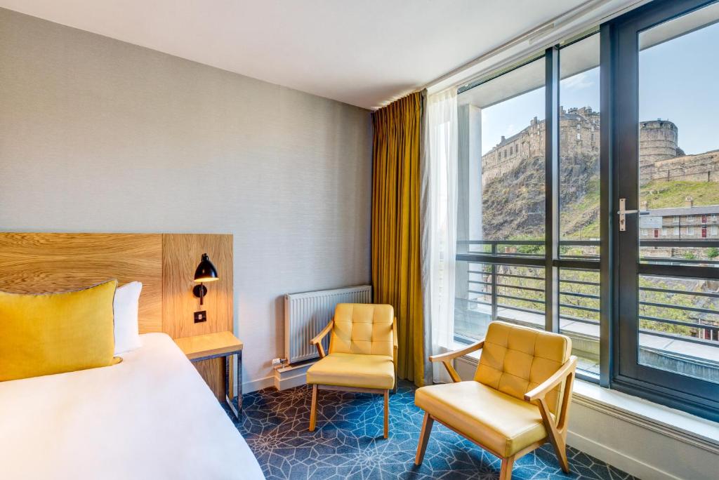 a hotel room with a bed and two chairs and a window at Apex Grassmarket Hotel in Edinburgh