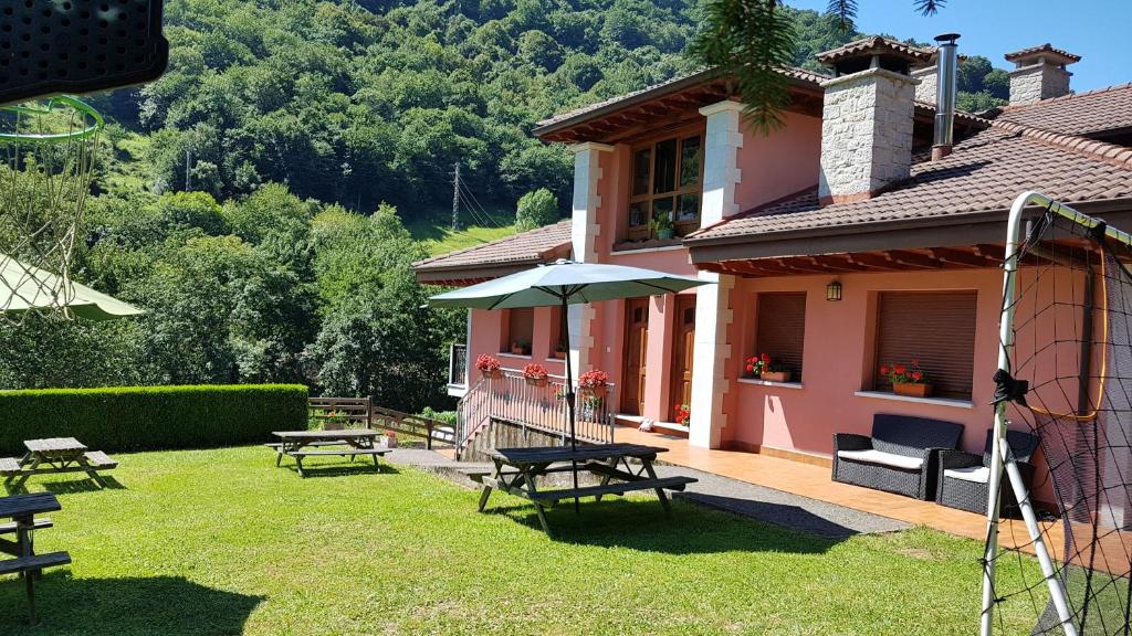 una casa con mesas de picnic y una sombrilla en el patio en Apartamentos La Corona - Cabrales, en Carreña