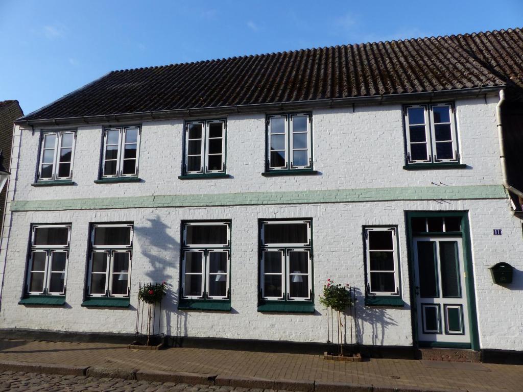 ein weißes Haus mit schwarzen Fenstern und grünen Rollläden in der Unterkunft Alter Krämerladen von 1732 in Friedrichstadt