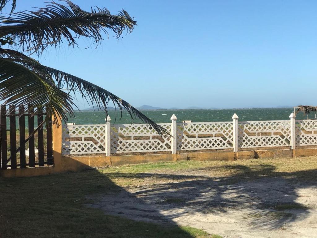 a white fence with a palm tree in front of it at Casa Frente Lagoa in Arraial do Cabo