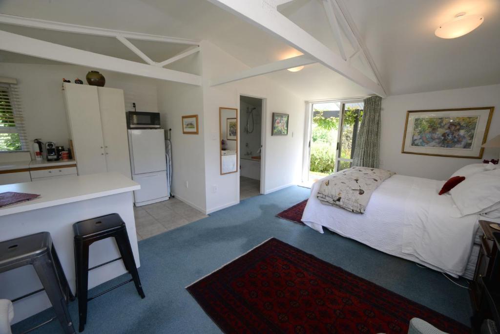 a bedroom with a white bed and a kitchen at L'abri Bed and Breakfast in Akaroa