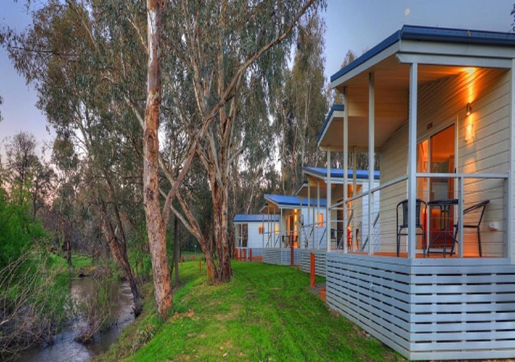 a white house with trees in front of a river at Yea Riverside Caravan Park in Yea