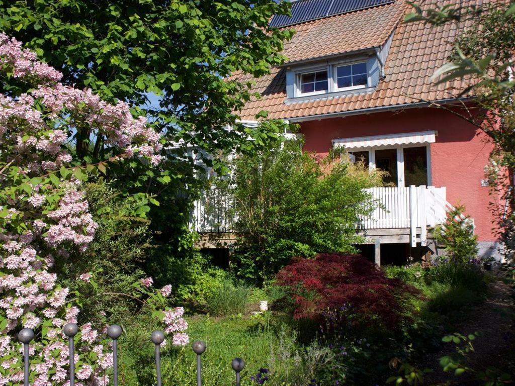 une maison rouge avec un jardin orné de fleurs roses dans l'établissement Ferienwohnung Brigid, à Uhldingen-Mühlhofen