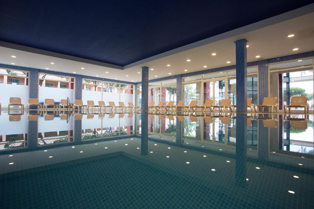 a room with chairs and a pool in a building at Hipotels Barrosa Garden in Chiclana de la Frontera