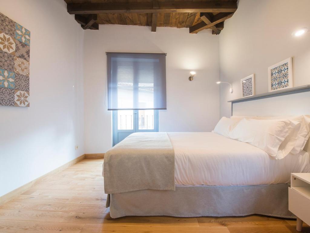 a white bedroom with a large bed and a window at Aldaba Apartamentos in Toledo