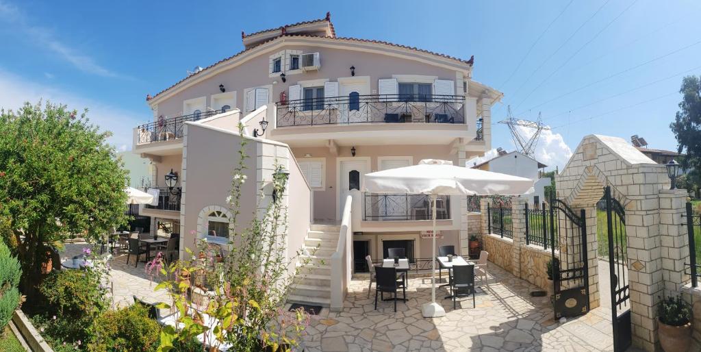 un grand bâtiment blanc avec des tables et un parasol dans l'établissement Villa Kormos, à Kavos