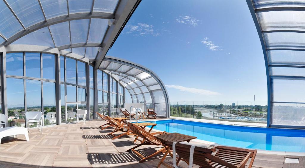 a swimming pool with chairs and a large glass ceiling at Westotel Le Pouliguen in Le Pouliguen